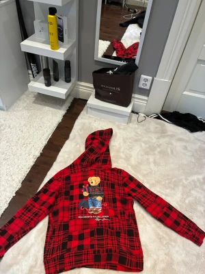 Röd rutig hoodie Polo Bear Ralph Lauren - Snygg röd och svart rutig hoodie från Ralph Lauren med Polo Bear-tryck på framsidan. Hoodien har en klassisk huva 
