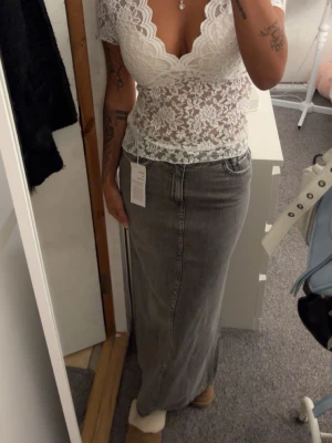 Grå långkjol i denim - Säljer en snygg grå långkjol i denim med klassisk rak passform. Kjolen har sömdetaljer framtill och en enkel, stilren look som passar till många olika outfits. Perfekt för dig som gillar en avslappnad men trendig stil.  Storlek 32 men passa mig som bruka ha i vanligt fall 34 i byxor