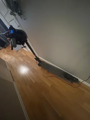 Svart elscooter med display - Elektrisk scooter i svart med digital display på styret och laddningskabel. Scootern har bred fotplatta och robusta hjul, perfekt för smidig transport i stan. Modern design och enkel att använda.