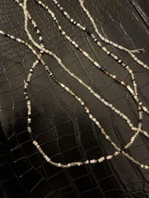 Flerfärgade maghalsband - Långt maghalsband med små pärlor i vitt, svart och brunt samt inslag av blått. Halsbandet har en tunn och flexibel design som gör det lätt att bära lager på lager. Perfekt accessoar för att addera lite färg och personlighet till din stil.