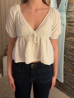 Vit v-ringad blus  - Hej!🌸Jag säljer en söt vit blus med v-ringning och korta puffärmar. Modellen är croppad med en lös passform och har en liten knytning framtill. Tillverkad i ett lätt bomullstyg som passar perfekt till jeans eller kjol.                                              Väldigt fin och sparsamt använd!🫶