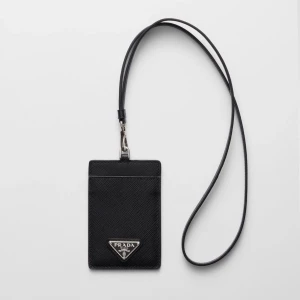 Svart korthållare - Minimalistisk svart korthållare med avtagbart band att ha runt halsen. Klassisk trekantslogga i silver framtill. Tillverkad i exklusivt skinn med stilren design, perfekt för kort och ID.