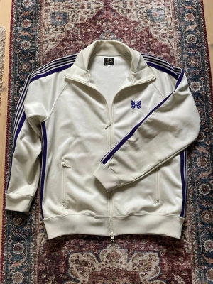 Needles track jacka - Krämvit och lila Trackjacket från Needles. Storlek L men sitter som M ungefär. Väldigt bekväm jacka med perfekt passform. Den har en missfärgning på insidan av kragen, men inget som syns när man har på sig den.