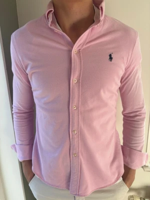 Rosa Ralph Lauren Featherweight Mesh Skjorta - Snygg rosa skjorta från Ralph Lauren i Featherweight Mesh. Riktigt go kvalitet! Passar perfekt nu till både vår och sommar. 🧵 Märke & Modell: Ralph Lauren 📏 Storlek: L men sitter  som en M/S. Vänligen mät noga! 🧩 Material: 100% ren bomull 📐 Mått: Axel 40 cm, armhåla 50 cm, ärm 64,5 cm, längd 69 cm ✅ Skick: 9/10. Väldigt fint skick! Bilderna talar. 🧍‍♂️Modellen (189 cm) bär den för tight. Passar en kortare!! Tips: Ta en skjorta du gillar och jämför måtten så det blir rätt. ‼️ Skickas iväg inom 24h ‼️