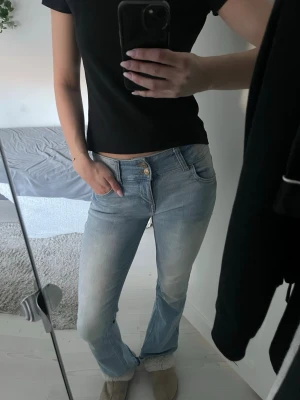 Ljusblå bootcut jeans - Säljer ett par ljusblå bootcut jeans med dubbla knappar i midjan. Jeansen har en lätt tvättad look och är perfekta för en avslappnad stil. Materialet är troligtvis bomull med mycket stretch för extra komfort samt är otroligt bekväma. Jag är 176 cm som referens. 