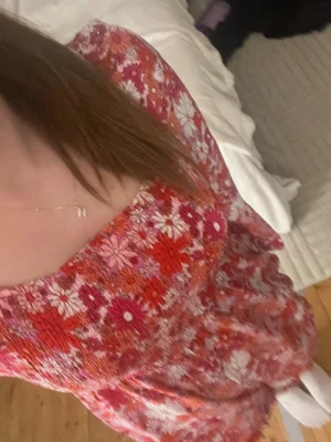 Blommig röd-rosa playsuit/shortsdress - Säljer en söt playsuit/shorts dress med blommigt mönster i rött, rosa, vitt och orange. Modellen har långa ärmar, markerad midja och fyrkantig ringning. Perfekt för dig som gillar färgglada och lekfulla plagg. Materialet känns lätt och luftigt.