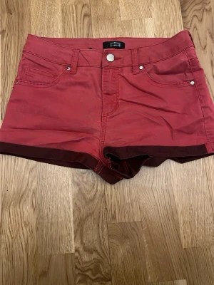 Röda shorts - Snygga röda shorts med hög midja och klassisk femficksdesign. Tillverkade i mjuk bomull med knapp och dragkedja framtill. Perfekta för varma dagar och enkla att matcha med olika toppar.