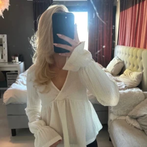 Vit v-ringad blus med volangärm - Snygg vit blus med v-ringning och långa volangärmar. Blusen har en lätt strukturerad yta och lös passform som ger en romantisk känsla. Perfekt att styla med jeans eller kjol för en trendig look.