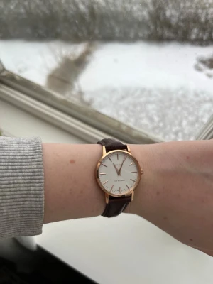 Gant klocka med brun läderrem - Stilren klocka från Gant med vit urtavla, guldfärgat boett och mörkbrun läderrem med krokopräglat mönster. Klassisk och tidlös design som passar till många olika stilar. Urtavlan har minimalistiska markeringar och tunna visare.