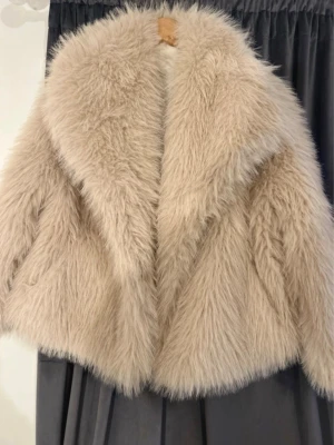 Beige fluffig pälsjacka - Supersnygg beige pälsjacka med oversized passform och bred krage. Jackan har långa ärmar och är gjord i ett mjukt, fluffigt material som ger en lyxig känsla. Perfekt för att hålla värmen under kalla dagar och ger en trendig look.