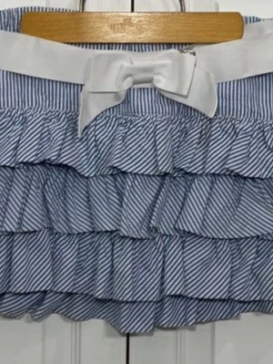 Polo Ralph lauren volangkjol med rosett - Söt kortkjol med blåvita ränder och flera volanger. Kjolen har en bred vit midjeresår och en stor rosett framtill för extra detalj. Perfekt för dig som gillar en lekfull och trendig stil.