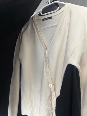 Stickad kofta  - Stilren vit kofta från Gina tricot med v-ringning och knäppning framtill. Koftan har långa ärmar och ribbad nederkant. Perfekt för lager-på-lager och enkel att matcha med olika outfits.