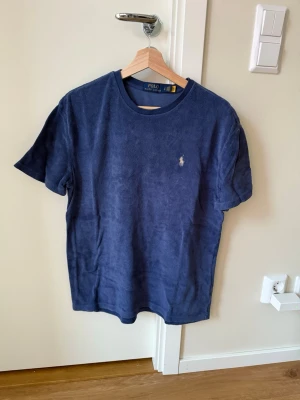 Blå t-shirt Polo Ralph Lauren - Blå t-shirt från Polo Ralph Lauren i mjukt material. Klassisk passform med korta ärmar och rund hals. Liten broderad logga framtill och stor Polo Ralph Lauren-tryck på ryggen. Sitter lite större.