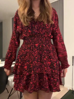 Röd och svart Zara klänning - Supersnygg kort klänning med röd och svart blommigt mönster. Klänningen har v-ringning, långa ärmar och markerad midja med volangdetaljer i kjolen. Perfekt för dig som vill sticka ut lite extra. Materialet känns lätt och flowy, troligen polyester.