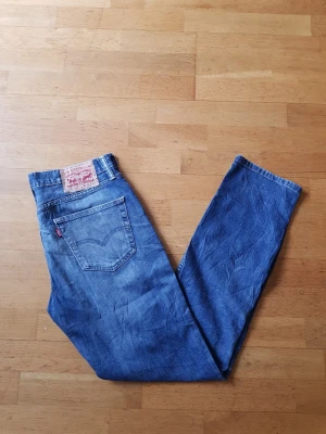 Levi's 511 blå jeans herr - Säljer ett par klassiska blå Levi's 511 jeans med rak passform och normal midja. Jeansen har fem fickor, Levi's ikoniska röda etikett på bakfickan och patch med logga i midjan. Tillverkade i slitstark denim av bomull. Perfekta för en avslappnad look.