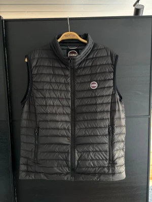 Svart dunväst från Colmar - Snygg svart dunväst från colmar. Västen är i storlek 52 vilket motsvara ungefär M. Det har lossnat liten på en sömm men inte man tänker på. Hör gärna av dig vid frågor. Mvh
