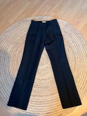 Svarta kostymbyxor från Nelly - Snygga svarta kostymbyxor från Nelly med raka ben och klassisk passform. Byxorna har hällor för bälte och diskret dragkedja framtill. Perfekta för en stilren look och passar till många olika outfits.