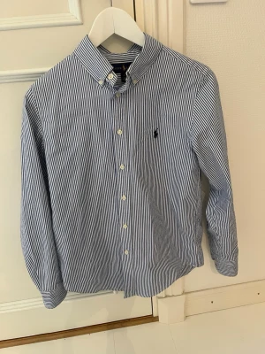 Blårandig skjorta från Polo Ralph Lauren - Säljer en klassisk blårandig skjorta från Polo Ralph Lauren med button-down krage och broderad logga på bröstet. Skjortan har långa ärmar, vita knappar och är tillverkad i bomull. Perfekt för dig som gillar stilrena och tidlösa plagg.