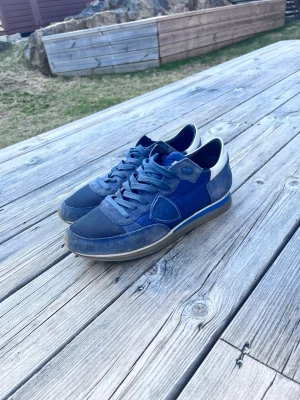 Blå sneakers från Philippe Model - Snygga blå sneakers från Philippe Model med en mix av mocka och textil. Skorna har gråblå snören, vit häl och klassisk låg profil. Perfekt för dig som vill ha en stilren och cool look till vardags.