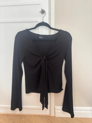 Svart långärmad topp Gina Tricot - Snygg svart långärmad topp från Gina Tricot med v-ringning och knyt framtill. På vänster ärm längst ner är det en liten limfläck men inget som syns på lite avstånd eller som stör. 