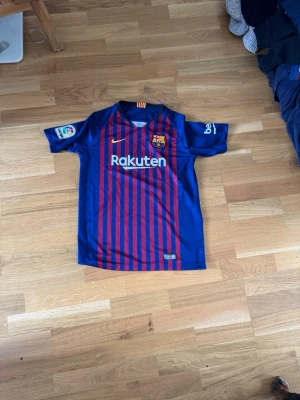 FC Barcelona matchtröja Nike 2018 - Säljer en officiell FC Barcelona matchtröja från Nike, säsongen 2018. Tröjan är blå med röda vertikala ränder, har klubbmärke, Nike-logga och Rakuten som sponsortryck. Tillverkad i lätt och ventilerande material, perfekt för fotboll eller träning. Kan ej se storlek men tror S