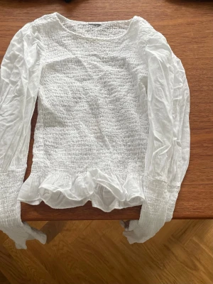 Vit smocktop - Vit kort smock top med lång puffärm. Rund halsringning och söt volang nedtill. Cool till jeans .