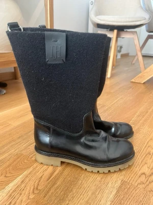 Svarta höga stövlar från Jil Sander - Unika svarta stövlar från Jil Sander med högt skaft i filt och nedre del i blankt läder. Grov beige sula för extra edge och cool look. Stövlarna har en stilren design med en stor logotypdetalj på skaftet. Perfekta för dig som vill sticka ut.