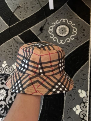 Beige bucket hat med rutigt mönster - Snygg bucket hatt för 200kr endast! Den är HELT oanvänd och jag har precis öppnat mitt paket och insåg att den var liten så därför säljer jag. Kan även vändas och vara svart hatt