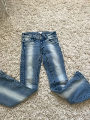 Blå bootcut jeans med slitningar - Snygga blå bootcut jeans med tydliga slitningar och ljusa partier framtill och baktill. Klassisk femficksmodell med dragkedja och knapp. Jeansen har en avslappnad passform och är tillverkade i denim.