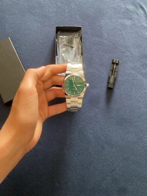Silverfärgad klocka med grön urtavla från poedagar. - Stilren klocka från poedagar med grön urtavla och dag/datumvisning. Armbandet är i silverfärgad metall. Perfekt accessoar för dig som gillar snygga detaljer. Justerare medföljer!!!
