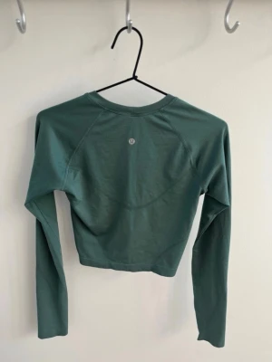 Grön croppad långärmad topp Lululemon - Snygg grön croppad långärmad topp från Lululemon. Tillverkad i ett mjukt och stretchigt material som passar perfekt till träning eller chill. Enkel design med rund halsringning och diskret logga på ryggen.