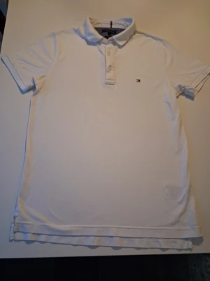 Vit pikétröja från Tommy Hilfiger - Klassisk vit pikétröja från Tommy Hilfiger med liten broderad logga på bröstet. Tröjan har korta ärmar, krage och knappar framtill. Perfekt till en clean och stilren look. Varan är i mycket bra skick i storlek M slim fit. Hör av dig vid frågor