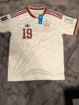 Vit Spanien fotbollströja Adidas - Spanien fotbollströja från Adidas med Lamine Yamal på ryggen. I färgen vit och vinröd Storlek L