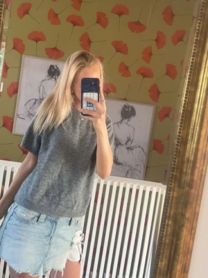 Grå stickad kortärmad topp - En enkel och stilren grå stickad topp med korta ärmar och rund hals. Perfekt att matcha med jeans eller kjol för en avslappnad look. Mjuk och bekväm, passar till många olika outfits.