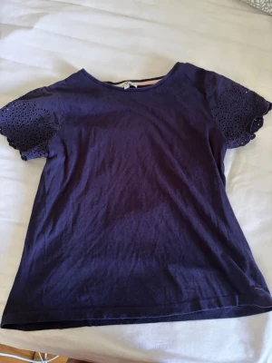 Mörkblå topp med spetsärmar - Snygg mörkblå topp med korta ärmar i broderad spets. Rund halsringning och mjukt bomullsmaterial gör den både bekväm och stilren. Perfekt för dig som vill ha en enkel men ändå unik topp med fina detaljer på ärmarna.