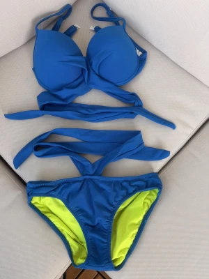 Blå bikini med knyt och neonfoder - Snygg blå bikini med vadderad topp och breda knytband som ger en trendig look. Underdelen har ett coolt neongult foder som sticker ut och gör bikinin extra unik. Perfekt för strandhäng eller poolparty!