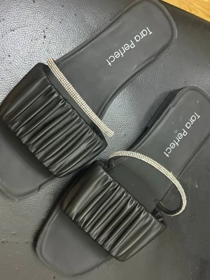 Tara Perfect Svarta Sandaler Storlek 39 - Svarta sandaler med en veckad rem över foten och en glittrig detalj. Skorna har en platt sula med ett mönstrat grepp undertill. Mycket bra skick som ny. Storlek 39. 