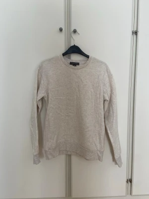 Beige sweatshirt - En vitspräcklig/beige sweatshirt med rund halsringning och långa ärmar. Tröjan har en skön bomullsblandning och ribbade muddar vid ärmslut och nederkant. Nopprig, därav lägre pris. 