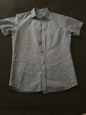 Ljusblå kortärmad linneskjorta - Snygg ljusblå skjorta från Jack&Jones i linne med korta ärmar och klassisk krage. Skjortan har knappar framtill och en avslappnad passform, perfekt för varma dagar. Enkel och stilren design som passar till mycket.  Använd på en skolavslutning förra året och inte använd sedan dess