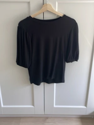 Svart topp med puffärm - Stilren svart topp med puffiga trekvartsärmar och rund halsringning. Tunn och mjuk känsla, perfekt att matcha till olika looks. Enkel men trendig design som passar till mycket.
