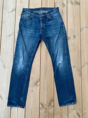Nudie Jeans Fearless Freddie - Ett par blå jeans från Nudie Jeans med raka ben, klassisk femficksmodell och slitna detaljer på knäna. Jeansen har orange kontrastsömmar, fransad kant nedtill och Nudie-logga på bakfickan. Tillverkade i denim med snygg tvätt.