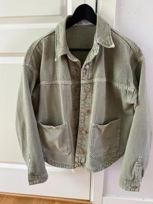 Olivgrön overshirt från Zara - Säljer en olivgrön overshirt från Zara i storlek S. Overshirten har två stora fickor framtill, klassisk krage och knäppning med tryckknappar. Tillverkad i ett kraftigare bomullstyg som ger en avslappnad och trendig look.