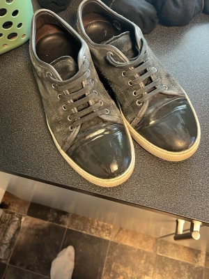 Gråa Lanvins - Snygga gråa sneakers med ovandel i mocka och svart lackad tå. Skorna har vita sulor och matchande gråa skosnören. Perfekta för dig som gillar en stilren men ändå unik look. Passar till det mesta och ger en cool touch till outfiten. Kvalitet 7/10