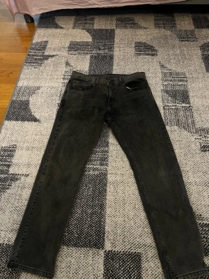 Levi's Jeans - Säljer ett par svarta raka jeans från Levi's med klassisk femficksmodell och läderpatch bak i midjan. Jeansen har en något tvättad look och är tillverkade i denim. Perfekta för dig som gillar en tidlös och avslappnad stil.