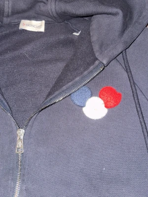 Moncler zip  - Säljer en riktigt äkta, fet Moncler hoodie som inte säljs längre, har en stor logga med röd vit och blå färg. Storlek M men sitter mer som S och passar dig 170+. Använd sparsamt inga märken eller trasigt någonstans, färgen är clean och inte urtvättad.
