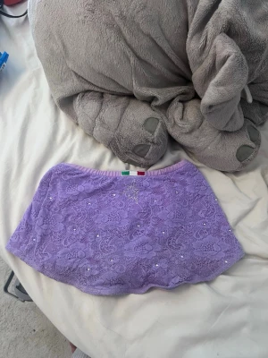 Ljuslila karisma/spetskjol med pärlor - En söt ljuslila karisma kjol med spets och små pärlor som dekoration. Kjolen har ett elastiskt midjeband och är fodrad under spetsen. Perfekt för dans, träning eller som ett statement-plagg till sportiga outfits.