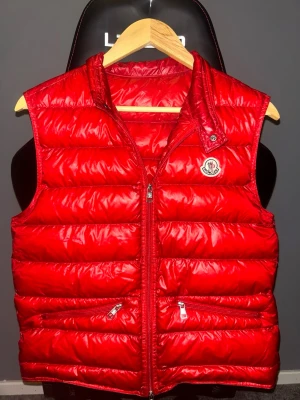 Äkta Moncler Väst Gui Röd Size 1 = XS-S - Säljer en moncler väst som jag köpte år 2019 från NK (Se sista bilden) då den är för liten. Den är 100% äkta, men den finns inte kvar på Monclers hemsida längre då den är lite OG nu. Västen är fylld med nedtvättade gåsfjädrar. NYPRIS: 8399kr hos NK. Skick: 9/10. Hör av dig om du har frågor eller vill ha fler bilder :)
