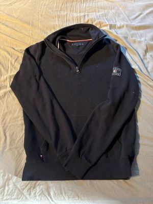 Svart halfzip från Tommy Hilfiger - Snygg svart hoodie från Tommy Hilfiger med halv dragkedja och klassisk logga på ärmen. Hoodien har en hög krage och mjukt material, perfekt för en chill och stilren look. Tvättar tröjan innan jag skickar iväg den ☺️tröjan är svart/blå färg.