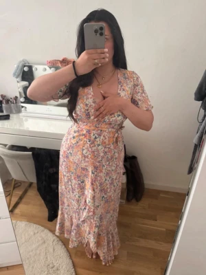 Blommig långklänning med volang - Fin sommarklänning. Det är en omlottsklänning satt man knyter den. Slits där framme. Använd några gånger, inga synliga defekter. 