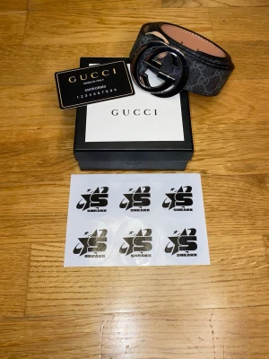 Svart GG Supreme bälte från Gucci - Snyggt svart bälte från Gucci med GG Supreme-mönster och stor GG-logga i metall som spänne. Bältet är gjort i skinn och har klassisk design med exklusiv känsla. Perfekt accessoar för att lyfta din outfit.